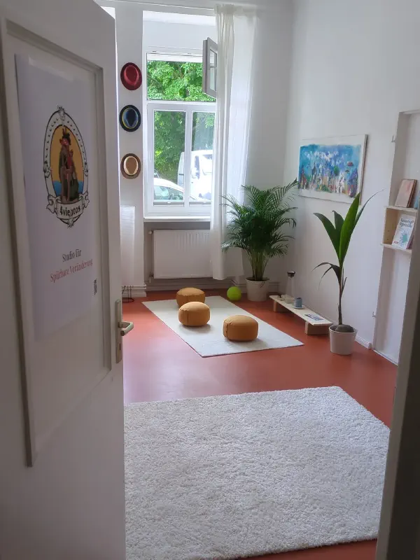 Blick durch die geöffnete Tür ins Studio mit Teppich, Kissen und Fenster