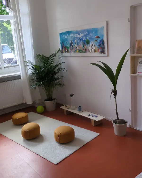 Meditationsecke im Studio: Sitzkissen auf hellem Teppich, Pflanzen und ein Gemälde an der Wand