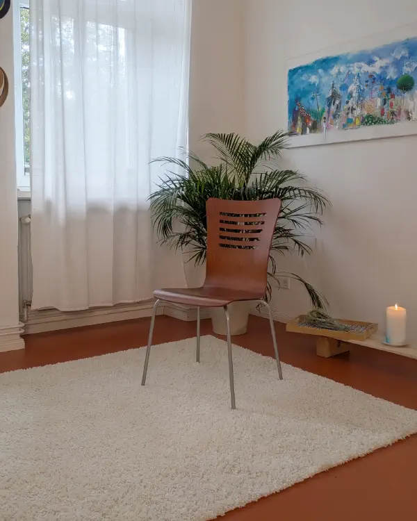 Ruhige Ecke im Studio: Stuhl vor großer Palme, daneben Kerze und Gemälde